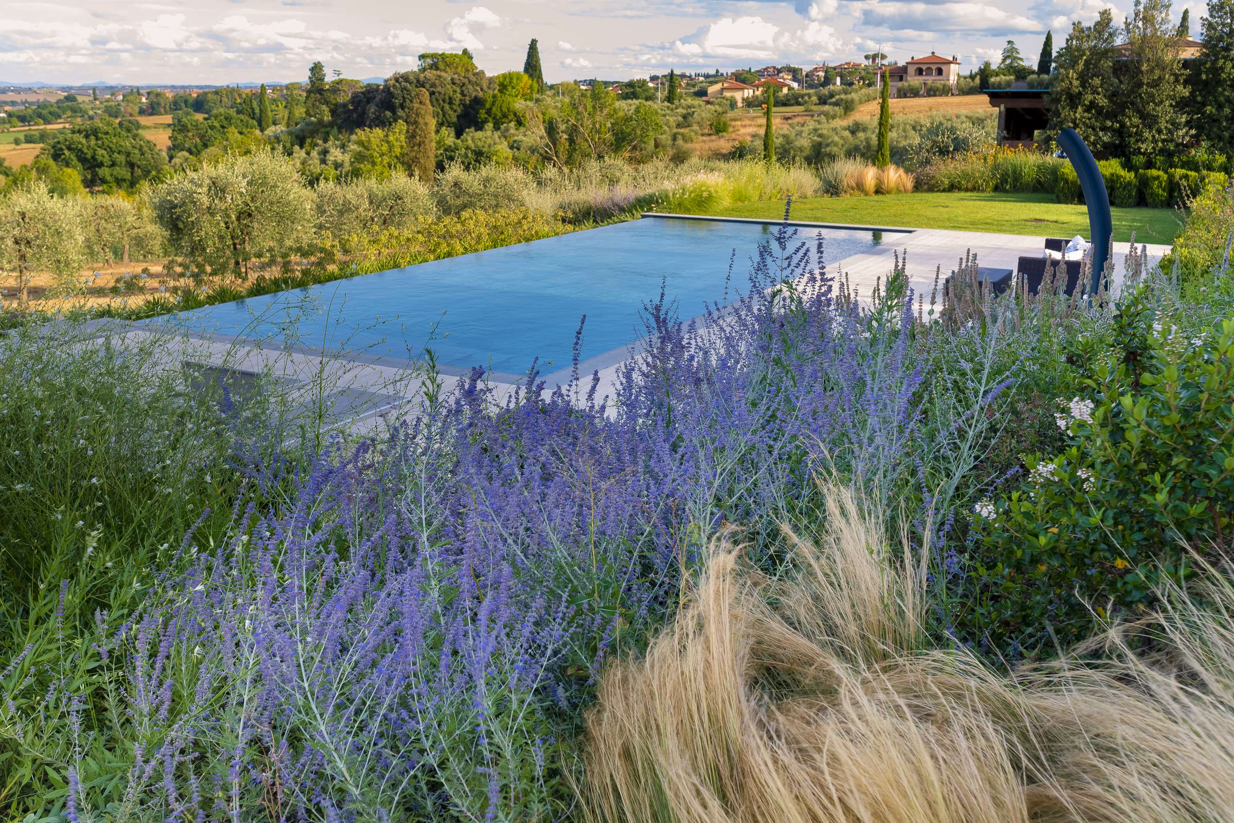 Piscina privata, realizzata in Toscana, con un lato a cascata e sfioro a fessura e una scala di design ad angolo