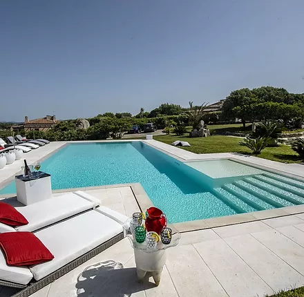 Piscina privata a sfioro Trilogy con scala e area relax interna, realizzata in Sardegna